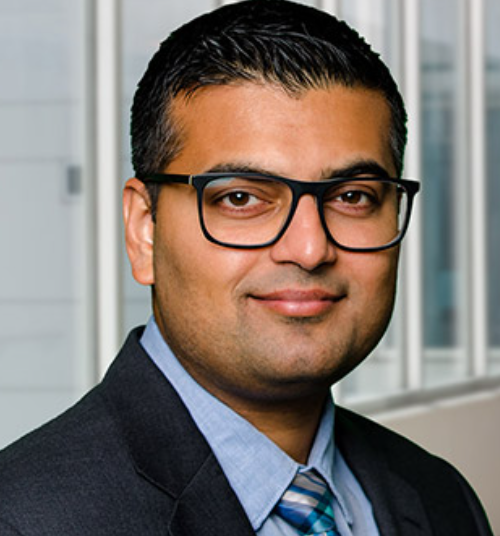 a man wearing glasses and a suit looks at the camera