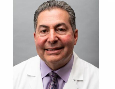 a man in a white coat and purple tie is smiling for the camera .