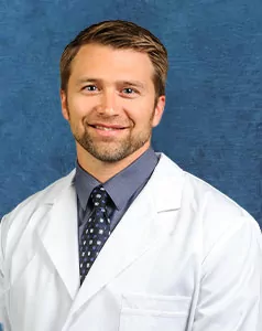 a man in a white coat and tie is smiling for the camera .