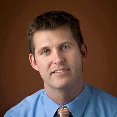 a man in a blue shirt and tie is smiling for the camera .